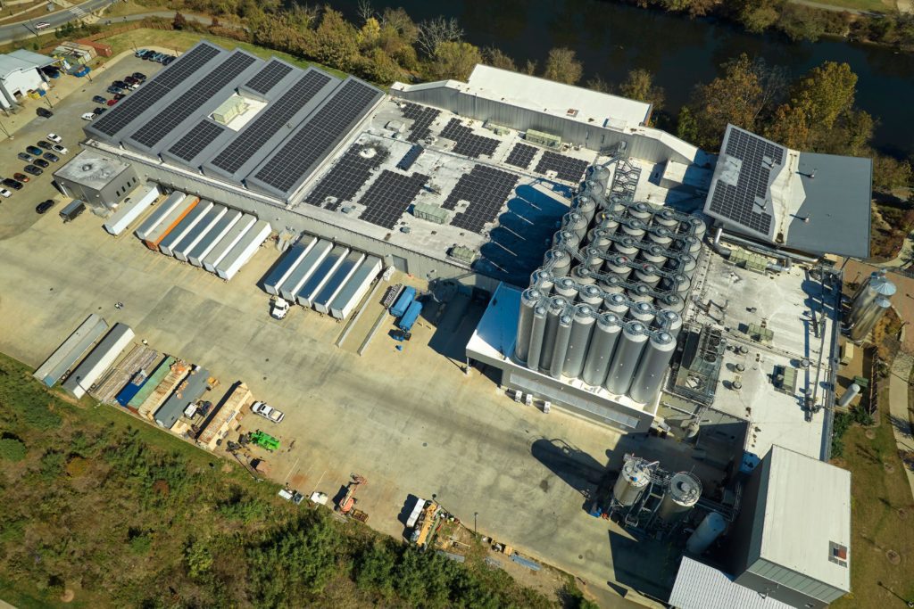 Aerial view of solar power plant with blue photovoltaic panels mounted on industrial building roof for producing green ecological electricity