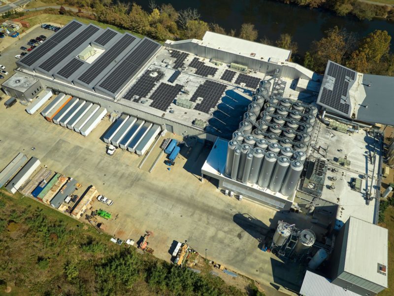 Aerial view of solar power plant with blue photovoltaic panels mounted on industrial building roof for producing green ecological electricity