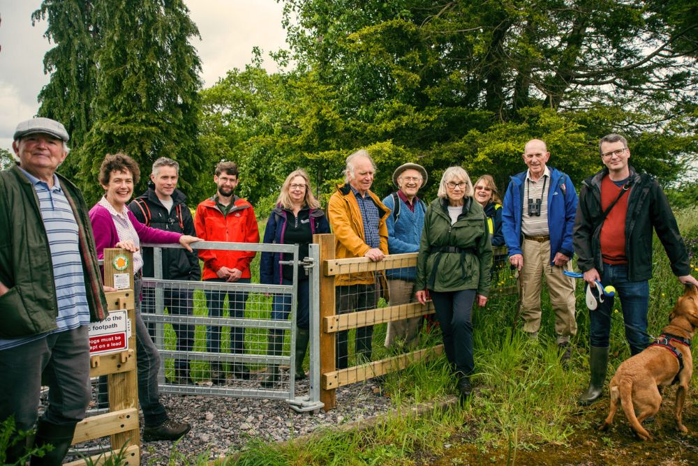 A group of people, and a dog, gather around an accessible gate, smiling to camera