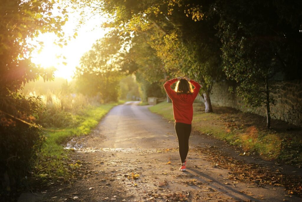 A young woman in a red jumper walking down a country lane with the sunset in the background