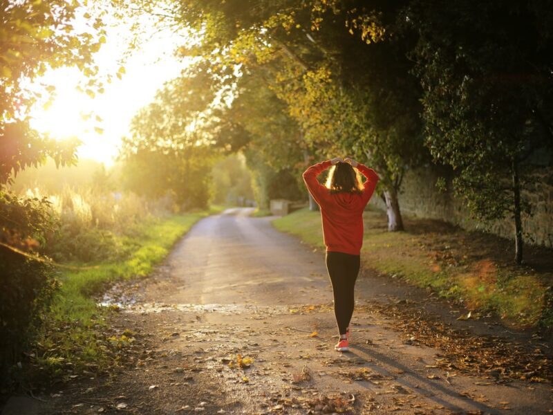 A young woman in a red jumper walking down a country lane with the sunset in the background