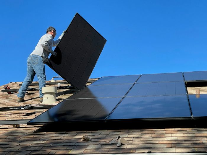 A man installing solar panels on a roof with blud sky behind