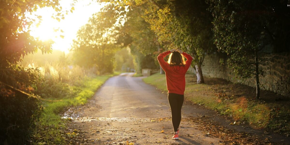 A young woman in a red jumper walking down a country lane with the sunset in the background