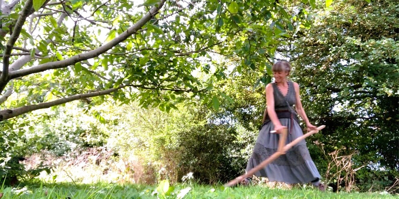 A woman scything wearing a long skirt and smiling